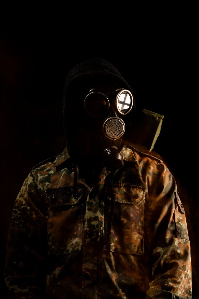 A person in a gas mask and camouflage jacket in darkness, evoking mystery and survival themes.